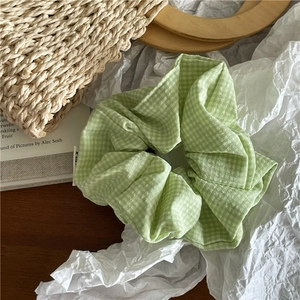 Détail d'un chouchou en tissu vichy vert clair sur un fond artistique minimaliste