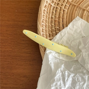 Detail view of a yellow hair clip with blue polka dots on a rustic wooden table