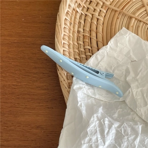 Detail of a light blue duckbill hair clip with white polka dots on a woven tray