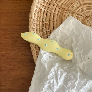 Detail of cream wave hair clip with blue polka dots on a minimalist textured surface