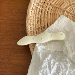 Close-up of cream wavy hair clip with blue polka dots on a natural wooden background