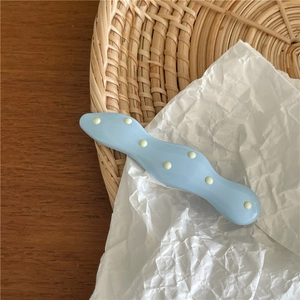 Close-up of wavy blue hair clip with yellow polka dots on a stylish textured background