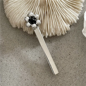 Détail d'une pince à cheveux fleurie argentée avec perle noire sur fond de pierre grise