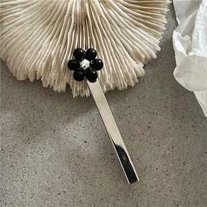 Gros plan d'une pince à cheveux argentée ornée d'une fleur en perles noires sur fond texturé