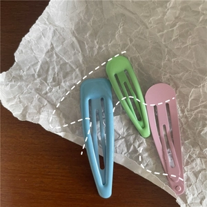 Close-up of three macaron-colored teardrop hair clips on a textured background
