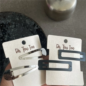 Set of four matte black rectangular and silver drop-shaped metal hair clips on a card