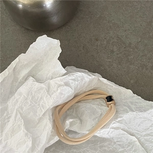 Dettaglio dell'elastico per capelli beige con fiocco in metallo dorato e intarsio nero