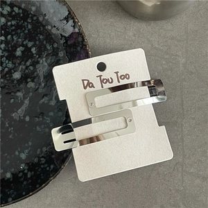 Detail of silver metallic rectangular hair clips set on a display card over a gray surface