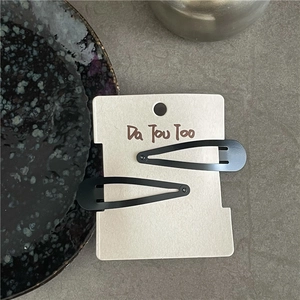Close-up of a pair of matte black teardrop metal BB hair clips on a display card