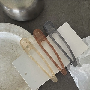 Three translucent acrylic hair clips in beige, amber and grey on a minimal card