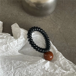 Détail d'un élastique spirale noir avec perle en résine marron sur surface en pierre