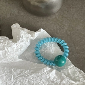 Détail d'un élastique spirale bleu avec perle verte sur fond de papier blanc