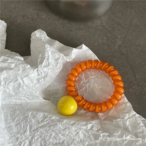 Détail de l'élastique à cheveux spirale orange avec un pendentif boule jaune brillant