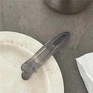 Detail of grey translucent hair clip with anti-slip teeth and metal spring on stone surface