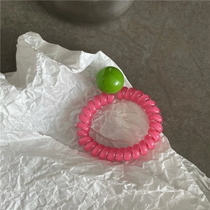 Élastique à cheveux spirale rose avec perle verte décorative sur papier blanc plissé