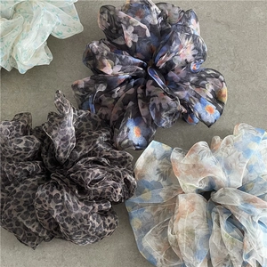 Close-up of sheer floral and leopard print mesh scrunchies on a stone surface