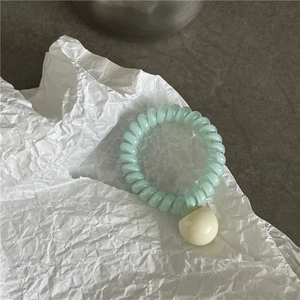 Détail d'un élastique spirale vert menthe avec une perle en résine crème sur papier blanc