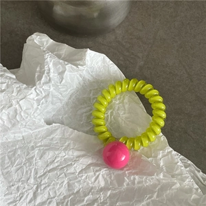 Détail de l'élastique spirale vert menthe avec perle rose sur papier blanc froissé