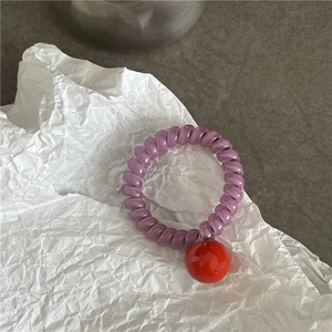 Gros plan sur un élastique à cheveux en spirale violet avec une perle bonbon rouge vif