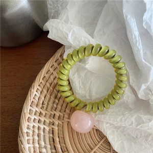 Détail d'un élastique spirale vert olive avec pendentif cœur rose sur plateau tressé