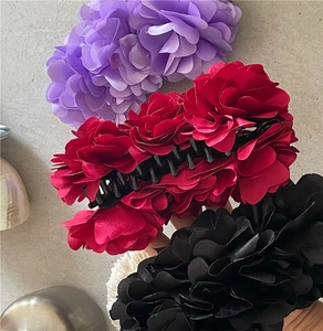 Macro view of large fabric flower hair clips in purple, red, and black satin texture