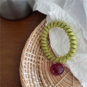 Gros plan sur l'élastique spirale vert avec perle rouge brillante sur un plateau tressé
