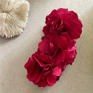 Close-up of three dark red fabric rose blossoms on a large elegant banana hair clip