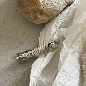 Detail of silver rectangular hair clip with wavy texture and metallic bead on stone