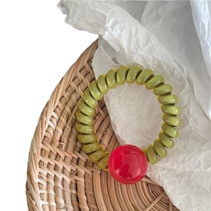 Élastique cheveux torsadé vert olive avec perle rouge brillante sur fond tressé