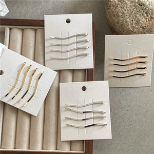 Dettaglio del set di 4 fermagli metallici a onda in oro e argento su cartoncino