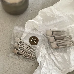 Close-up of handmade matte silver metal wavy hair clips set in transparent packaging