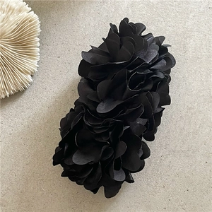 Detail of a large black satin fabric flower hair claw clip with a 3D multi-layer design