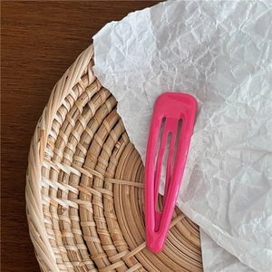Gros plan d'une barrette BB goutte en métal rose fuchsia sur un fond texturé naturel