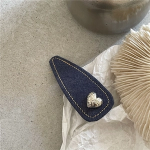 Detail of denim blue fabric drop hair clip with silver heart metal and yellow stitching