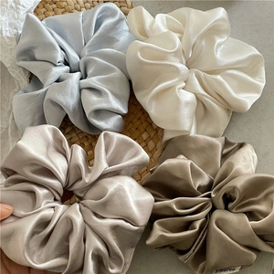 Detailed view of large satin scrunchies in blue, beige, gold, and bronze silk textures