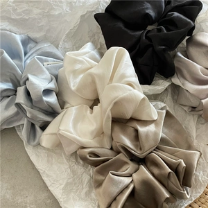 Detailed texture of assorted silk satin scrunchies in blue white black and champagne colors