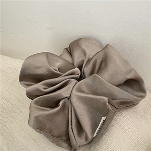 Close-up of champagne silk satin scrunchie with brand woven label on soft fabric
