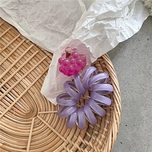 Dettaglio dell'elastico a spirale viola con ciondolo a uva rosa su vassoio intrecciato