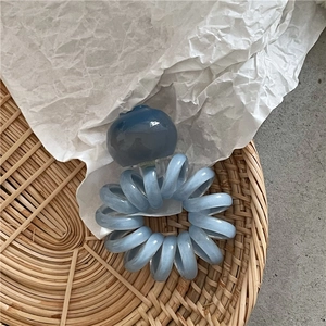 Dettaglio macro di un elastico a spirale azzurro con ciondolo a forma di bacca traslucida