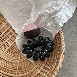 Dettaglio di un elastico per capelli a spirale nero con una perlina in resina rosa trasparente