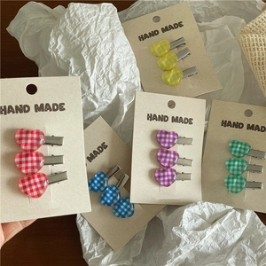 Close-up of heart-shaped checkered hair clips in five colors on handmade packaging
