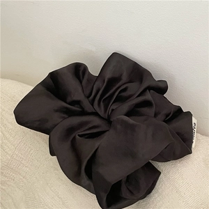 Detailed close-up of large black satin scrunchie with silky texture and woven label