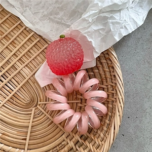 Dettaglio di un elastico a spirale rosa con ciondolo a forma di fragola su vassoio tessuto
