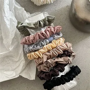 Close-up of seven assorted satin scrunchies with elegant pleats on a clear stand