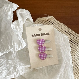 Detailed view of three purple gingham heart hair clips on a handmade card display