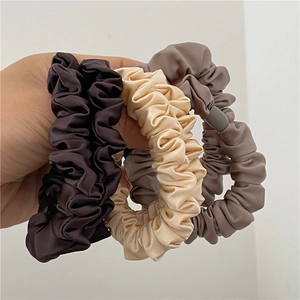 Close-up of three satin scrunchies in brown, cream, and taupe with pleated texture