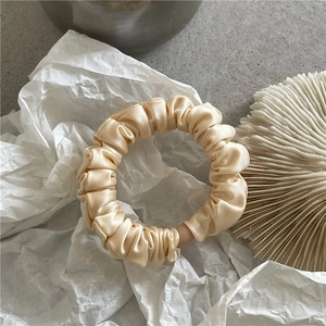 Close-up of cream satin scrunchie showing glossy silk texture and pleated detail