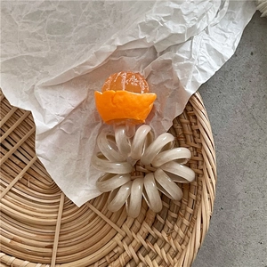 Dettaglio di elastico a spirale con ciondolo arancione in resina su cordoncino beige