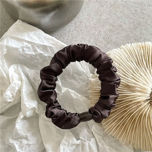 Detail of a brown satin scrunchie with smooth silk texture and a decorative oval bead