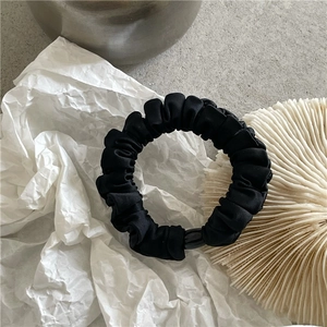 Detail of black pleated satin hair scrunchie with glossy cylindrical buckle on textured background